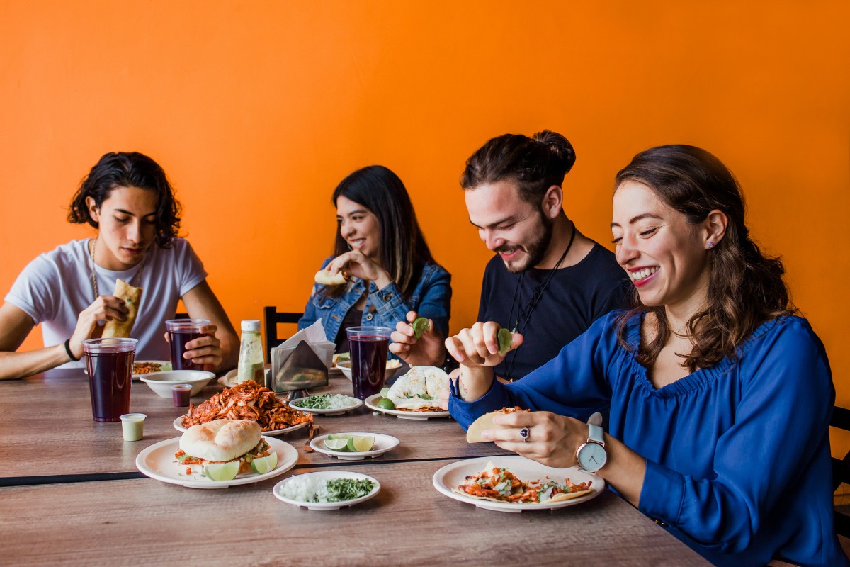 How Do Spicy Foods Affect Gum Health Four people enjoying a meal together at a table against an orange background.