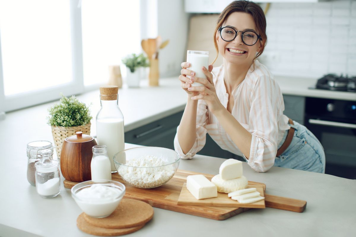5 Snacks that are Good for Your Teeth Woman in kitchen holding dairy products with milk, cheese, and yogurt displayed on counter.