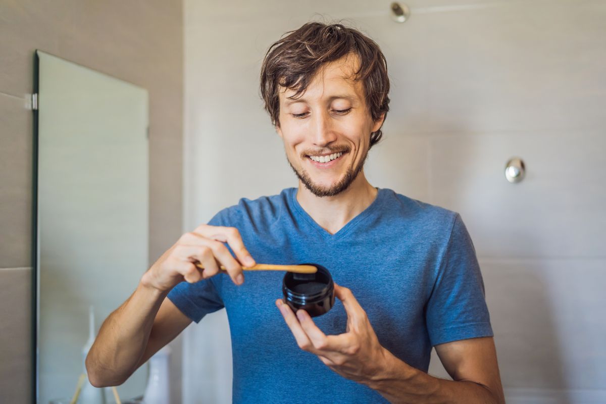 Can You Whiten Your Teeth Naturally Man in blue shirt holding dental aligners in modern office setting, smiling at camera.